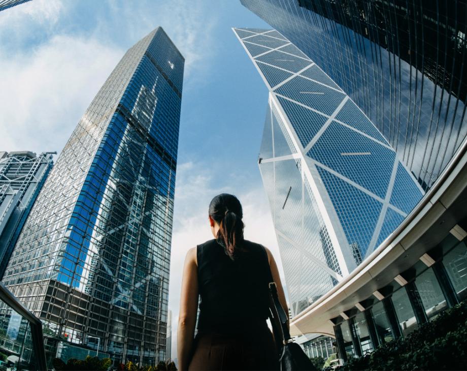Color photo of the back of a woman looking up at skyscrapers